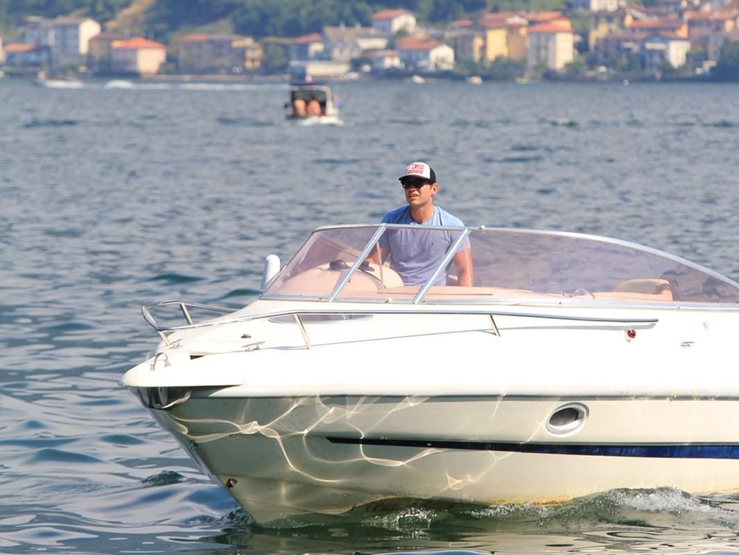Skipper Paolo standing at the helm of a Cranchi motorboat on Lake Como, photographed from the dock with a lakeside village behind