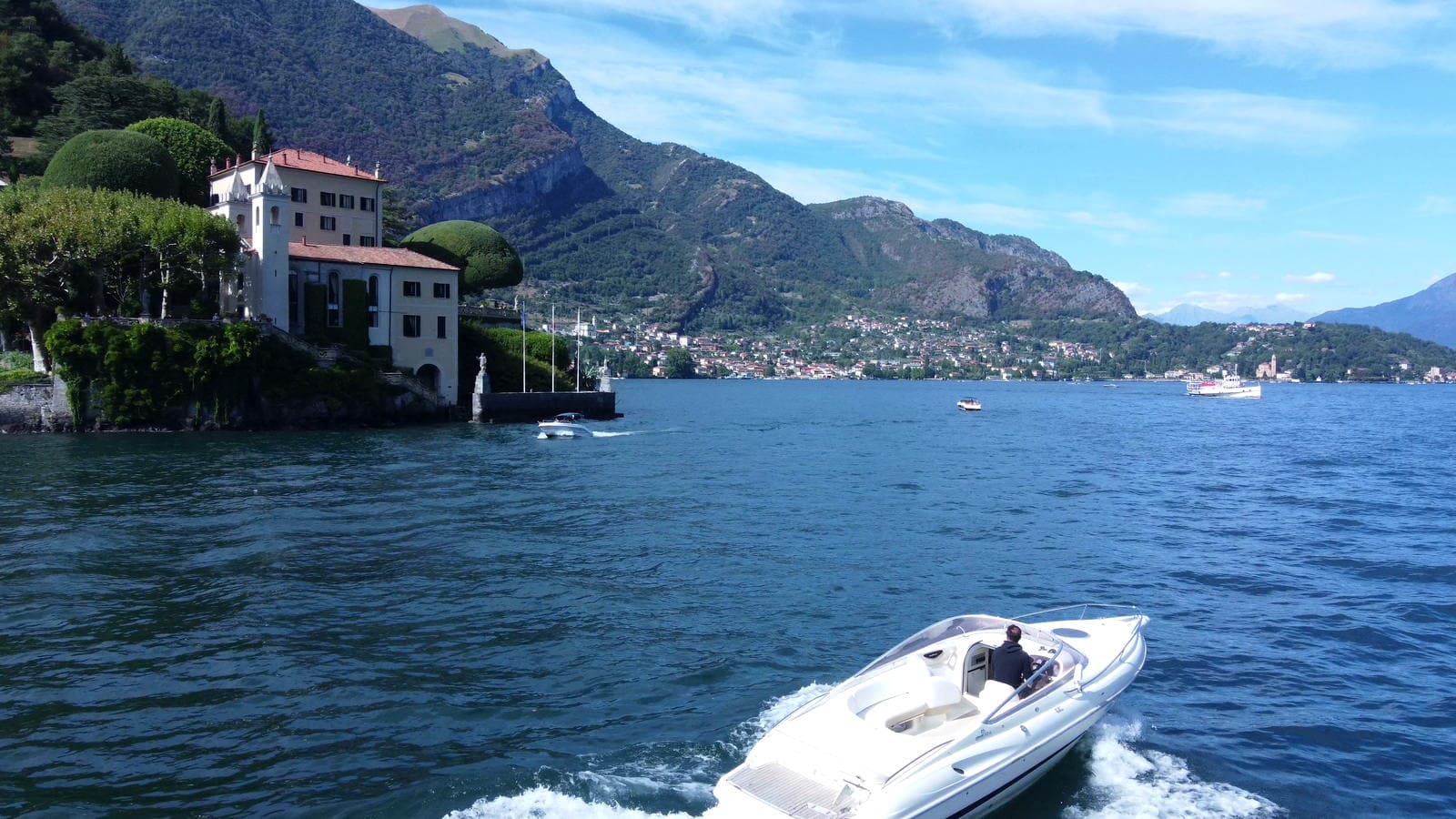 Villa del Balbianello above its stone landing on Lake Como, the private boat cruising past on open water