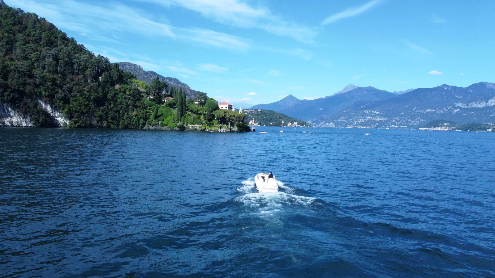 The private boat alone on open water on Lake Como, the far shore and the mountains behind it