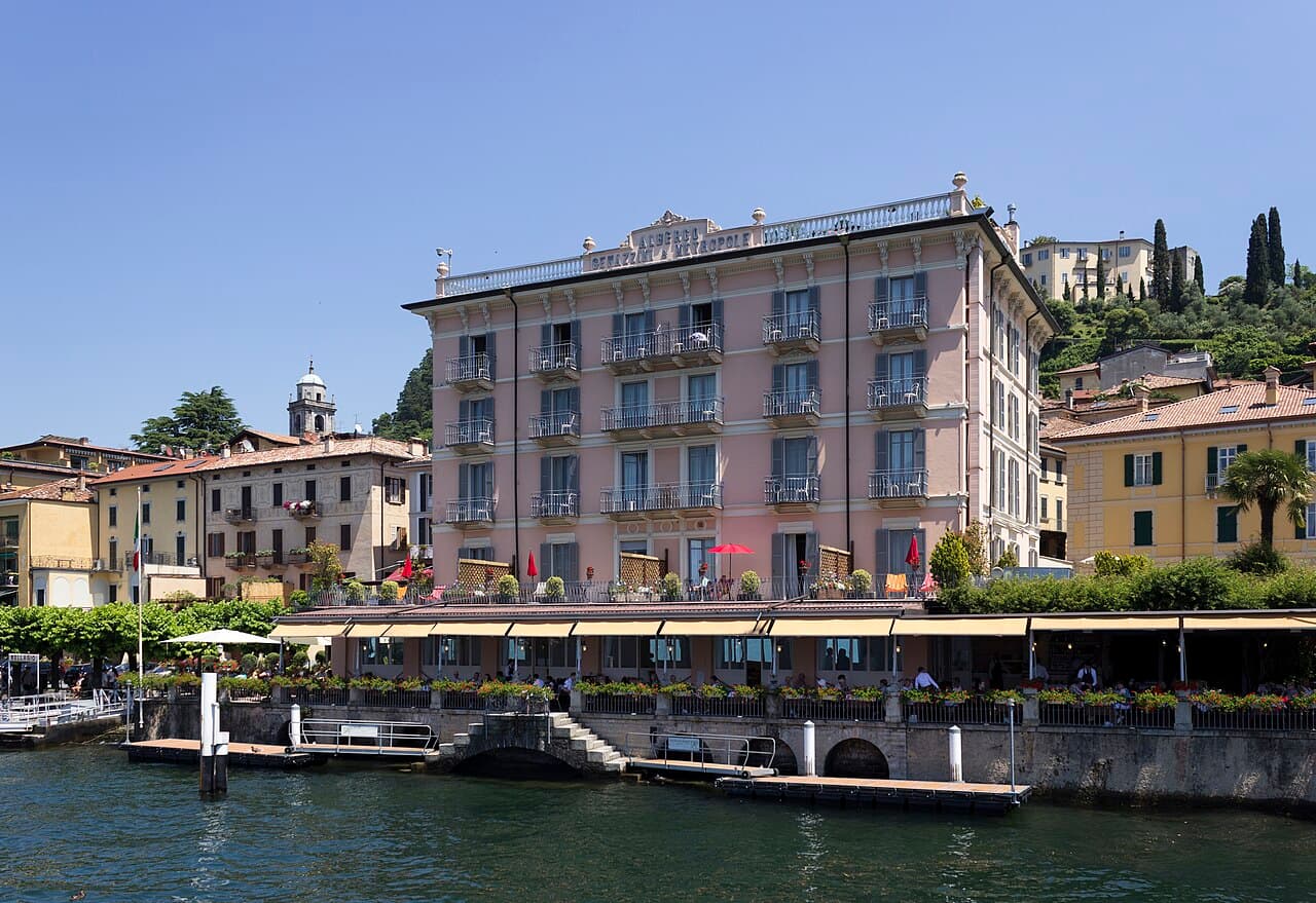 A private Cranchi motorboat cruising past a lakeside villa on Lake Como, with a public ferry visible in the distance