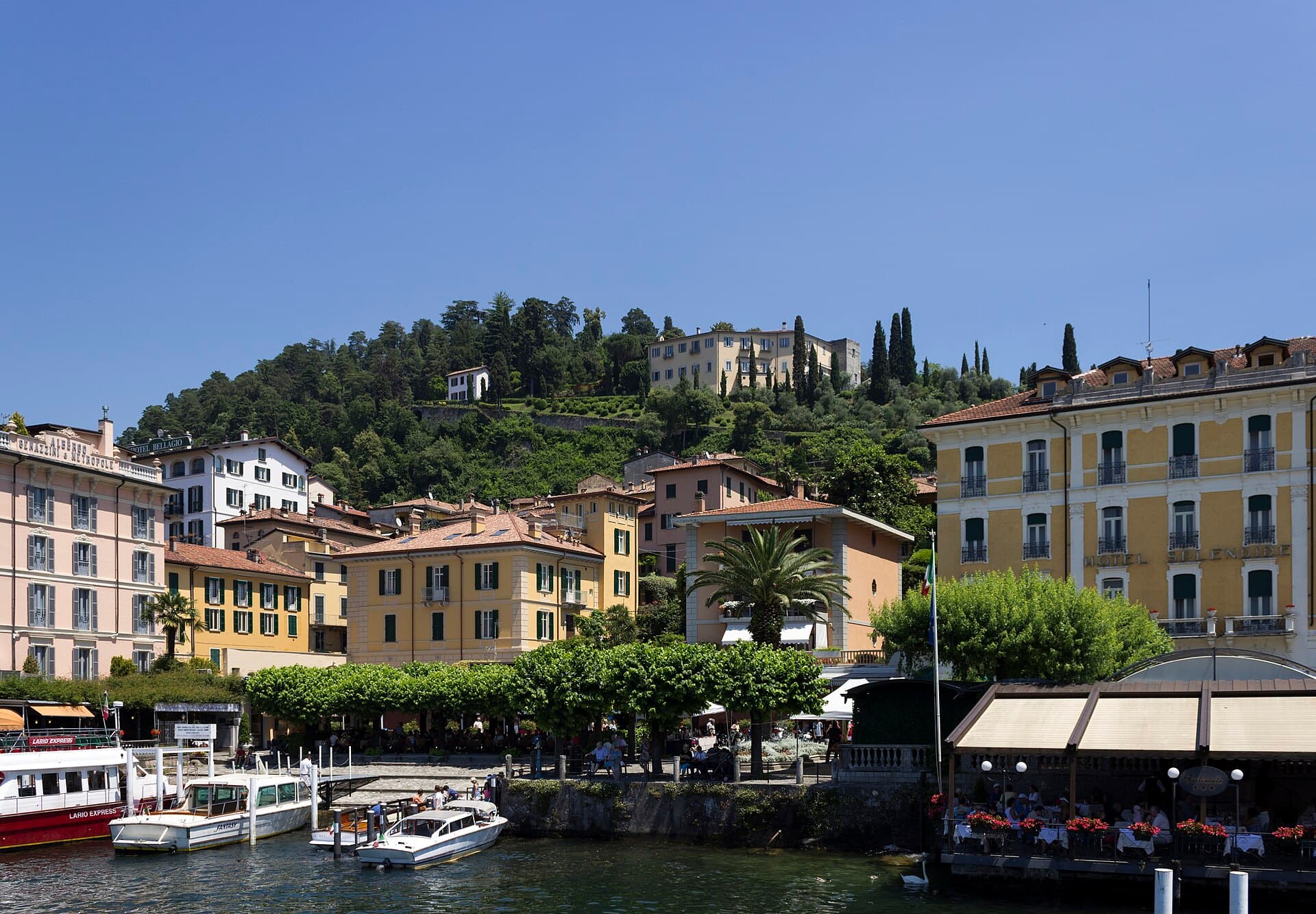 A private Cranchi motorboat cruising past a lakeside villa on Lake Como, with a public ferry visible in the distance