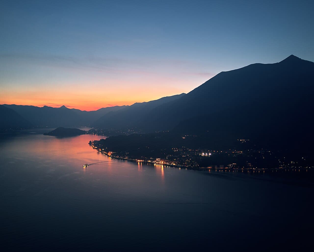 A private wooden Cranchi boat on the calm central waters of Lake Como at golden hour, warm sunlight on the mountains behind Villa del Balbianello