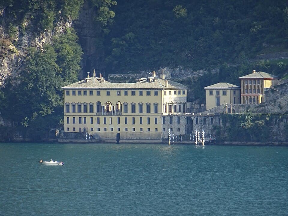 A couple embracing on a private boat on Lake Como at golden hour, with Villa del Balbianello in the background